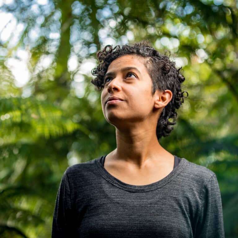 A woman with medium tone skin and short curly hair looks upwards in hope.