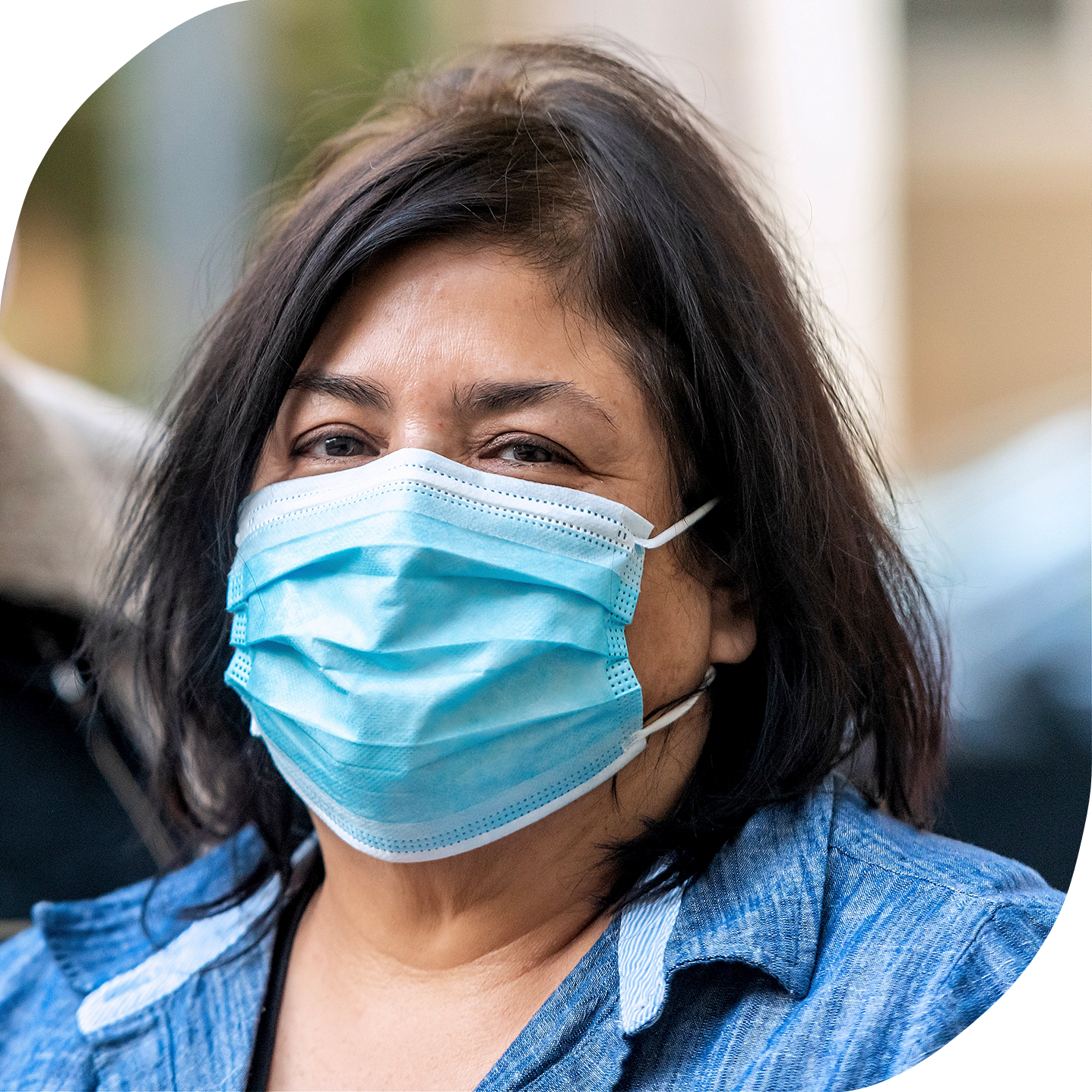 A middle-aged Asian woman wearing a light blue medical mask is looking into the camera.