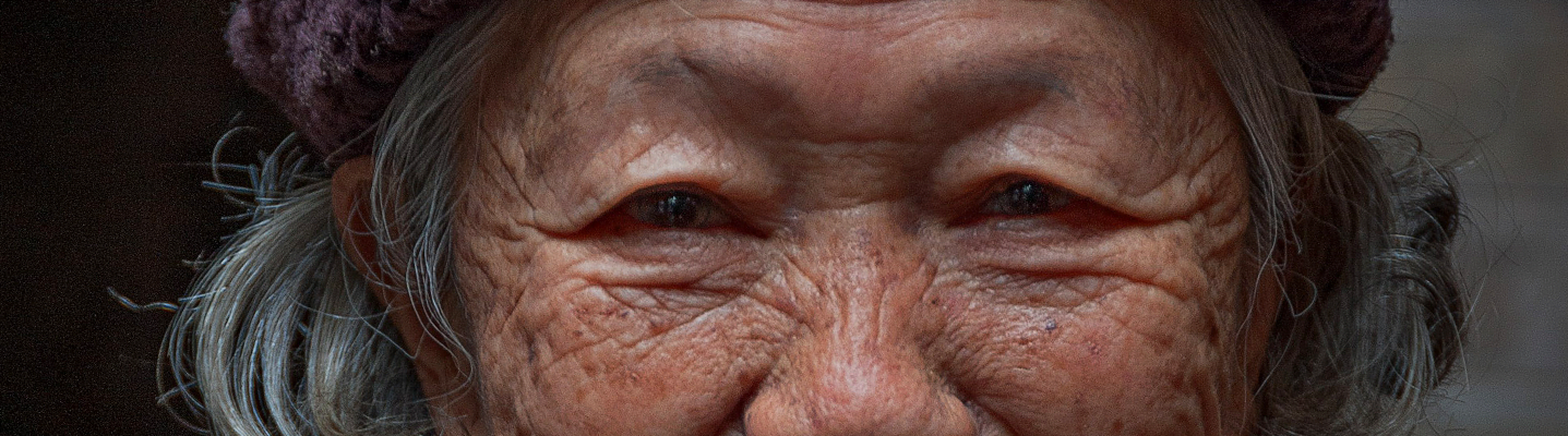 An elderly Asian woman wearing a knit cap is looking into the camera