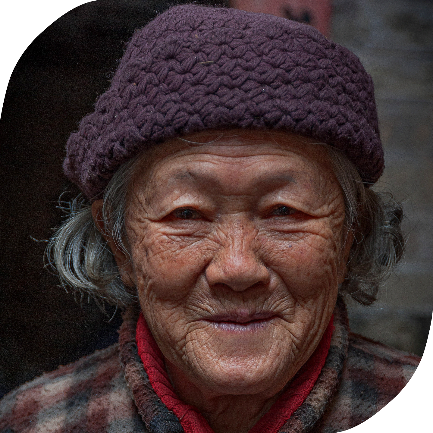An elderly Asian woman wearing a knit cap is looking into the camera