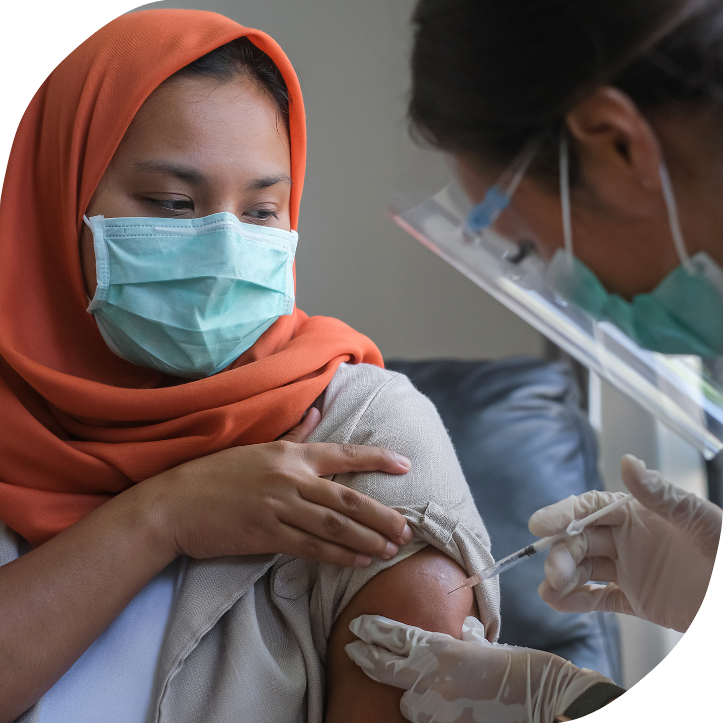 A young woman wearing an orange hijab is receiving her vaccine.