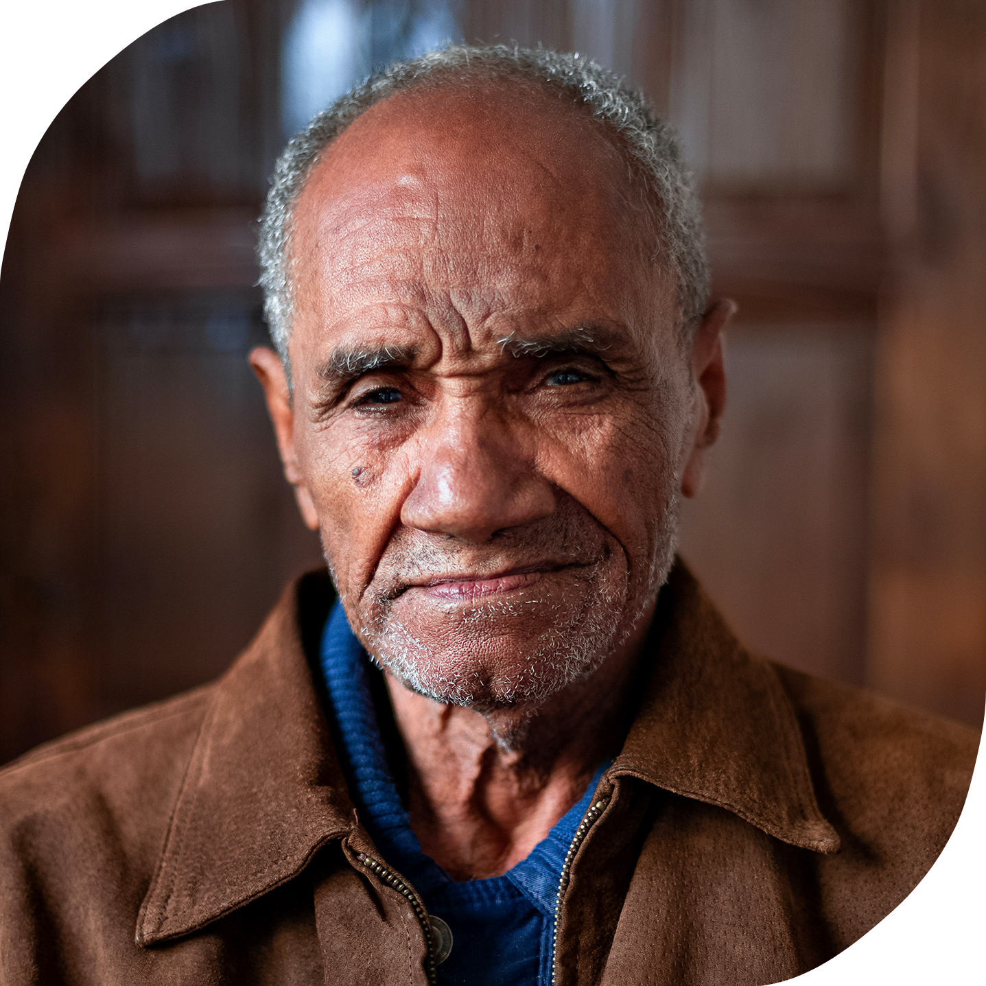 An older Black man with a weathered and wise face is looking into the camera.