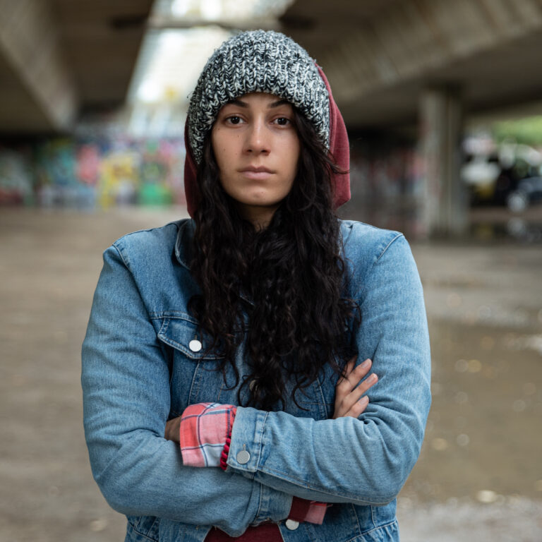 Young homeless woman standing alone under a bridge on the street in cold weather