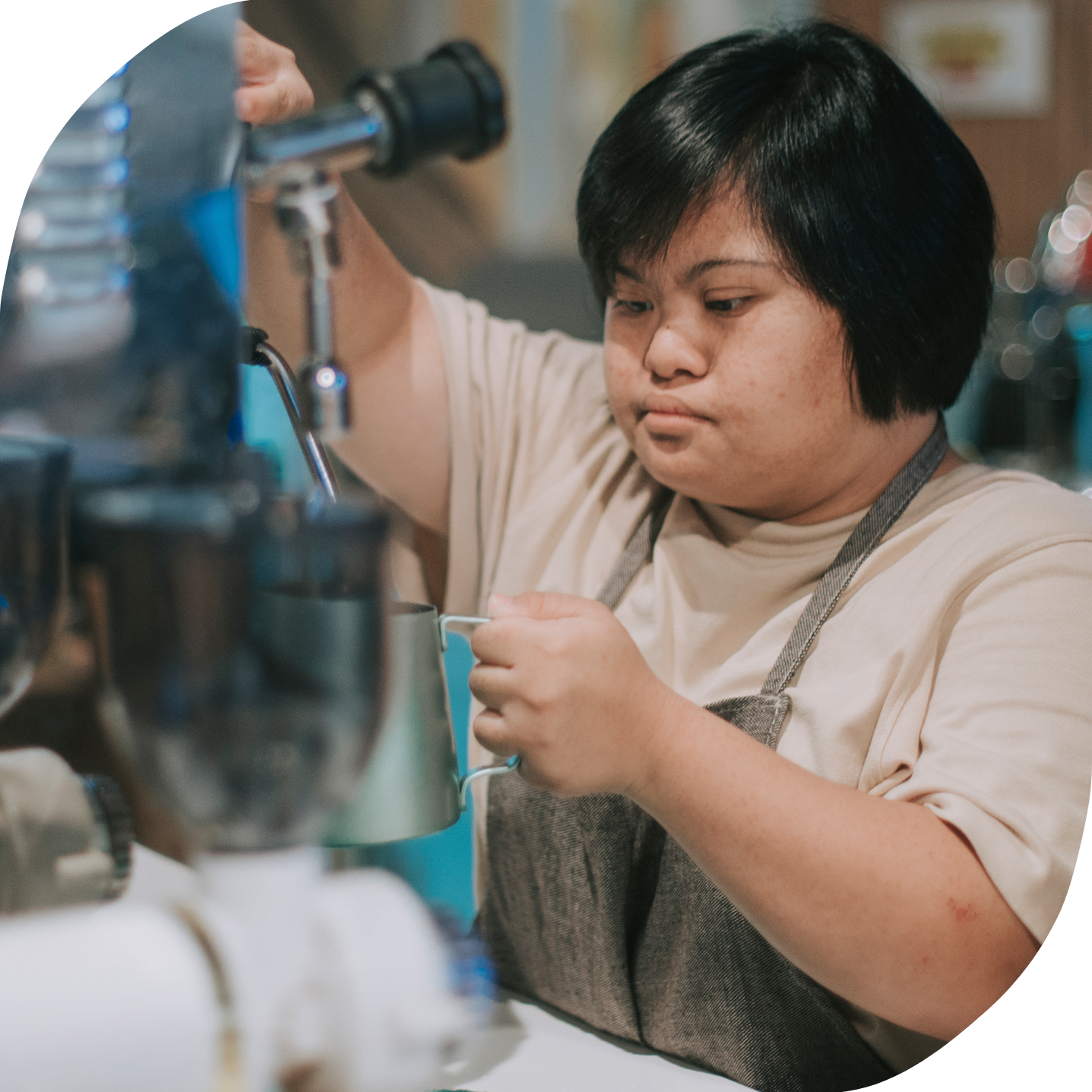 An Asian woman with down syndrome is working as a barista at a cafe. She is making a coffee.