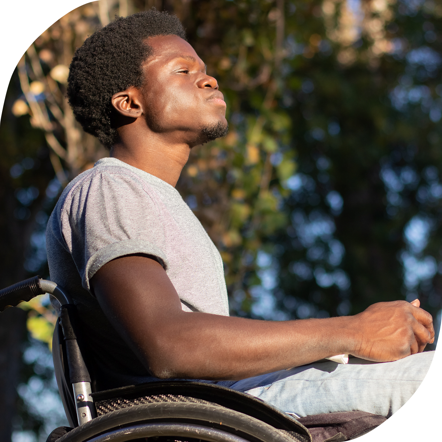 A young Black man in a wheelchair, outside on a sunny day.