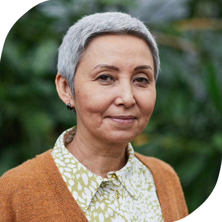 A woman with short grey hair who is wearing an orange cardigan over a green and white printed blouse.