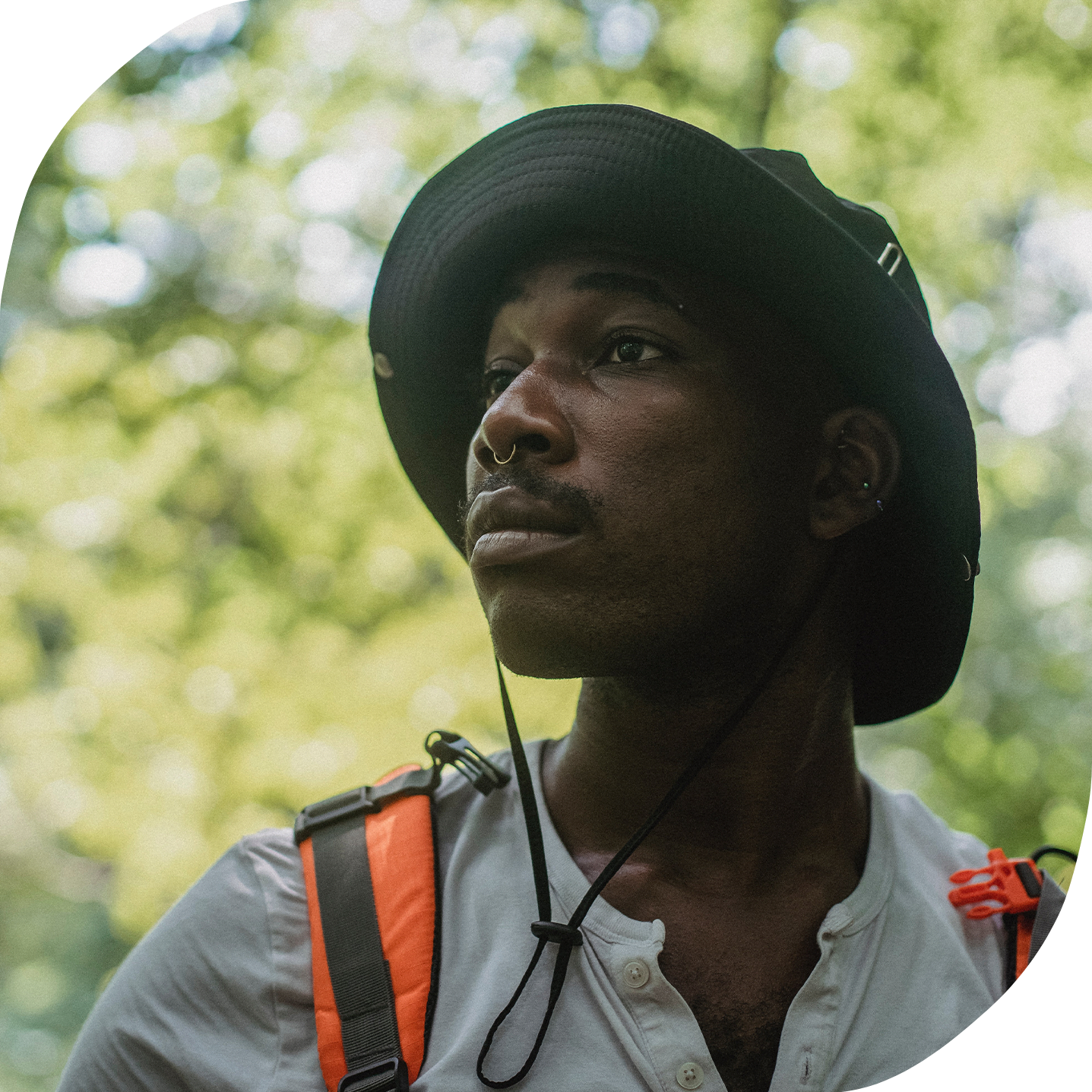 A close-up portrait of a Black non-binary person wearing hiking gear outdoors. They have a serious expression on their face.