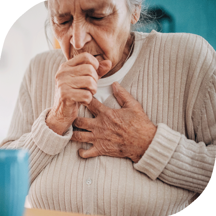 Elderly woman coughs into her right hand. Her other hand clutches her chest.